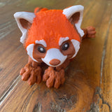 Orange Brown and White 3D printed Red Panda. Designed by Matmires and printed by Pilola. Shown on a wooden background Lying down with close up of head and face