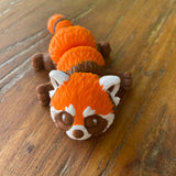 Orange Brown and White 3D printed Red Panda. Designed by Matmires and printed by Pilola. Shown lying down on a wooden background facing the front