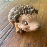 3D printed brown Hedgehog. Designed by Matmires and printed by Pilola. Showing a close up of it’s cute face on a wooden background 