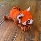 Orange Brown and White 3D printed Red Panda. Designed by Matmires and printed by Pilola. Shown on a wooden background Lying down looking to the right