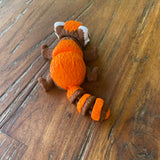 Orange Brown and White 3D printed Red Panda. Designed by Matmires and printed by Pilola. Shown on a wooden background Lying down showing it’s back and bushy tail